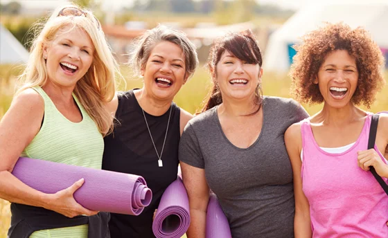 A portrait of a group of mature female friends, smiling at the camera, carrying yoga mats.